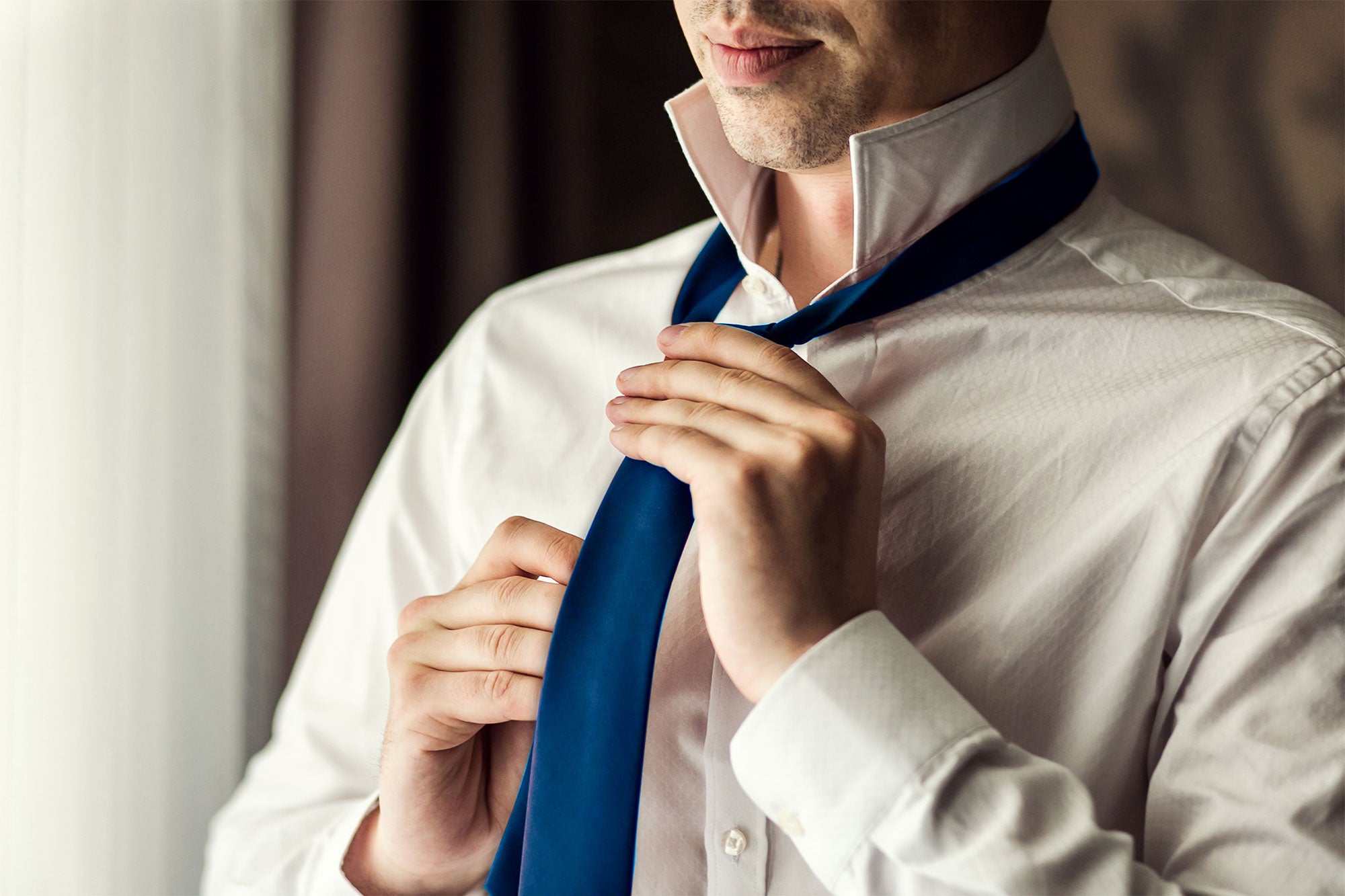 Man putting on a navy blue satin tie
