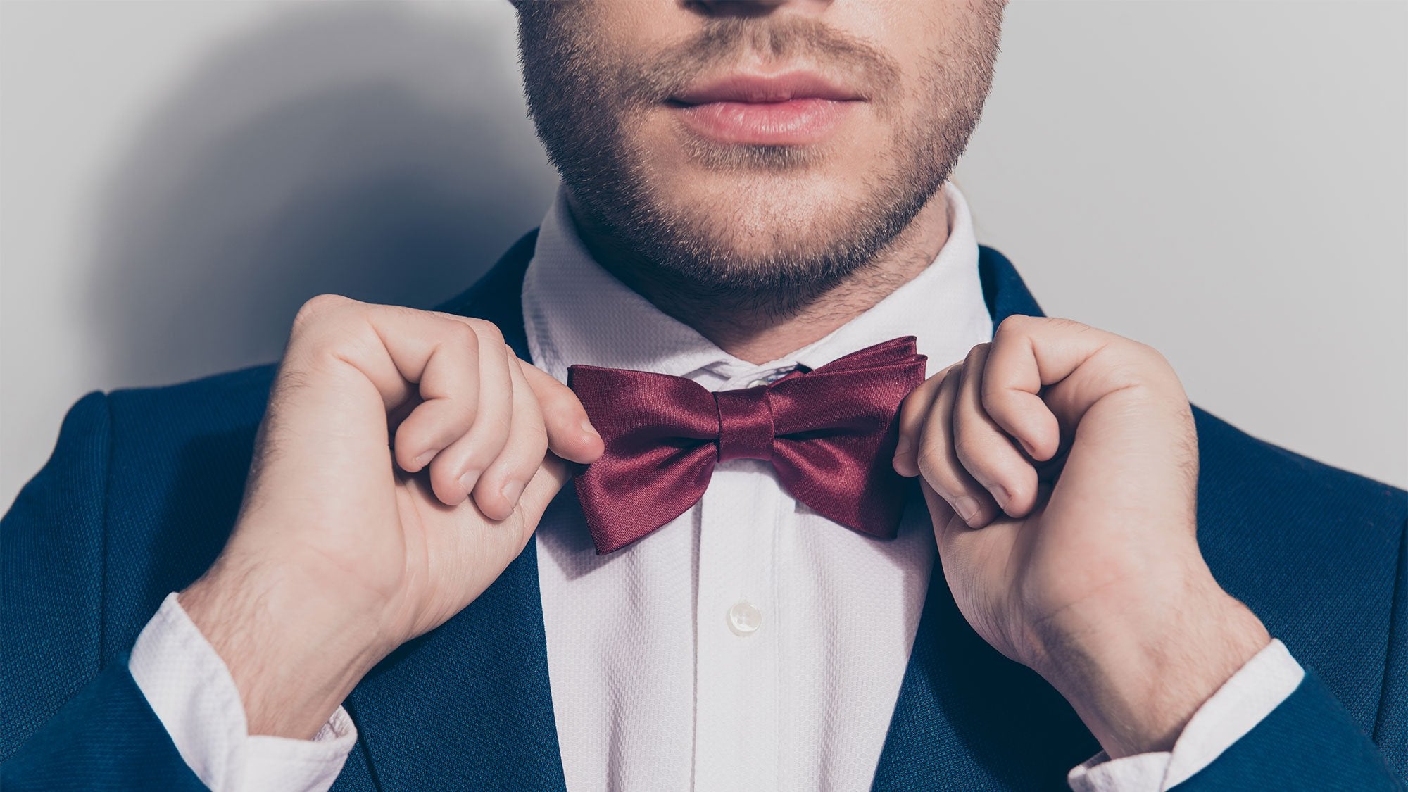 A man putting on a burgundy satin bow tie